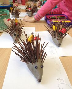 two hedgehog sculptures sitting on top of a wooden table next to paper and pencils