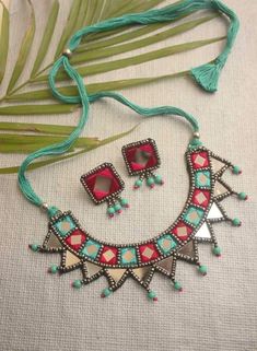 a necklace and earring set with beads on a white cloth table next to palm leaves