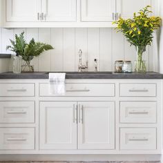 a kitchen with white cabinets and black counter tops, yellow flowers in vases on the sink