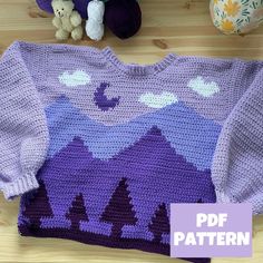 a crocheted sweater with mountains and trees on it, next to stuffed animals