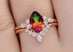 a woman's hand holding a ring with an orange, green and red stone