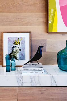 a black bird sitting on top of a white table next to vases and books