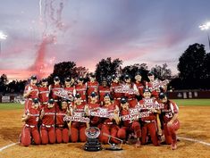 a group of women's softball players posing for a team photo with their trophy