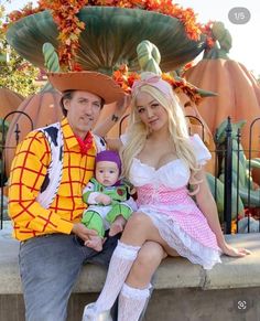 a man and woman in costumes sitting next to each other on a stone wall with pumpkins behind them