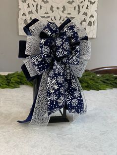 a blue and white snowflaked bow on a black stand in front of a christmas tree