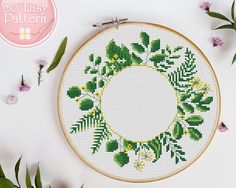 a cross stitch wreath with green leaves and flowers on white background next to pink flowers