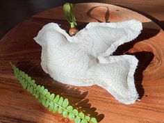 a white cloth on a wooden plate next to a green fern leaf and an object that looks like it has been made out of yarn