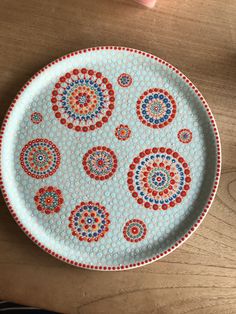 a white plate with red, blue and green designs on it sitting on a wooden table