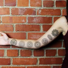 a woman's arm with tattoos on it and a brick wall in the background