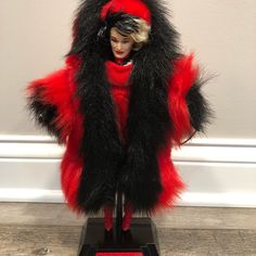 a red and black fur coat on top of a wooden stand next to a white wall