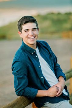 a young man sitting on top of a wooden fence next to the ocean with his arms crossed