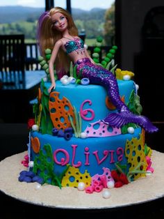 there is a cake that has a mermaid on the top and under it, as well as other decorations