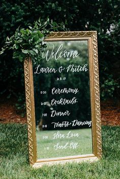 a wedding welcome sign in front of a gold framed mirror with greenery on top