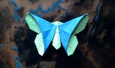 an origami butterfly sitting on top of a black surface with blue and green designs