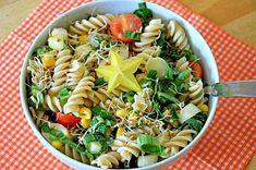 a white bowl filled with pasta salad on top of a checkered table cloth next to a fork