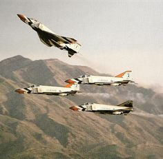 four fighter jets flying in formation with mountains in the background