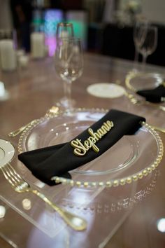 there is a black napkin on top of the glass place setting with silverware and wine glasses