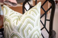 two pillows sitting on top of a black chair next to a table with a white and green pillow