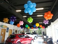 colorful balloons are hanging from the ceiling in a car showroom