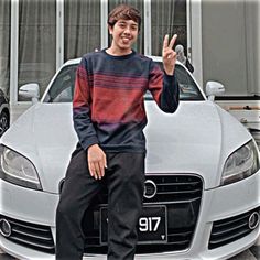 a man sitting on top of a car giving the peace sign with his hand in front of him