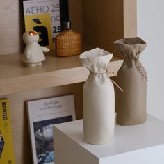 two white vases sitting on top of a shelf next to each other in front of books