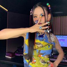 a woman with long black hair holding her finger up to her mouth while standing in front of a computer desk