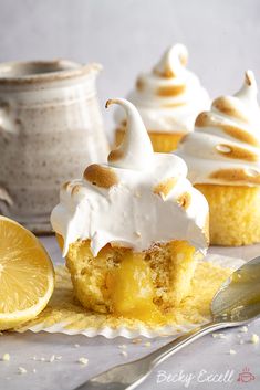 some cupcakes with icing and lemon on a white plate next to a spoon