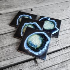 three coasters that have been painted with blue and green designs on them, sitting on a wooden surface