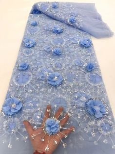 a person's hand on top of a blue table cloth with flowers and beads