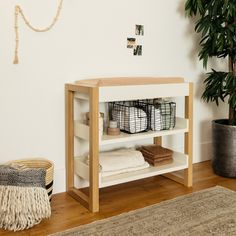 a white shelf with baskets and towels on it next to a potted plant in a room