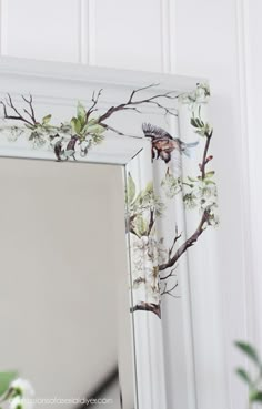 a white mirror with an image of a bird and flowers on it, sitting next to a potted plant