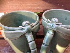 two green planters sitting next to each other on a wooden table, one with handles