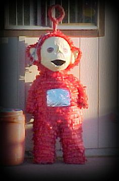 a teddy bear made out of plastic wrapped in red string and sitting next to a door