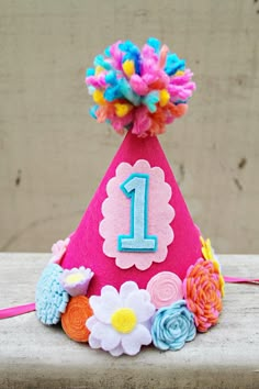 a pink birthday hat with flowers on the front and number one on the side, sitting on top of a table