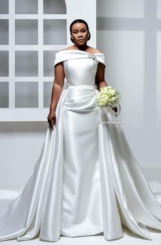 a woman in a white wedding dress holding a bouquet and posing for the camera with her hands on her hips