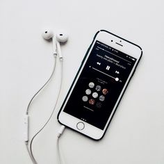 an iphone with ear buds connected to it sitting next to headphones on a white surface