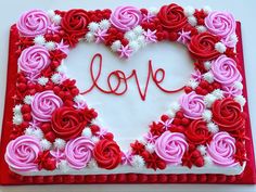 a heart shaped cake decorated with pink and red flowers on a white tablecloth that says love