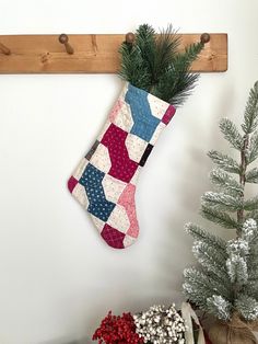 a christmas stocking hanging on the wall next to a potted plant and pine tree