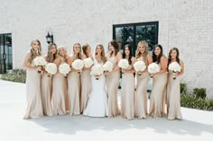 a group of women standing next to each other in front of a brick building holding bouquets