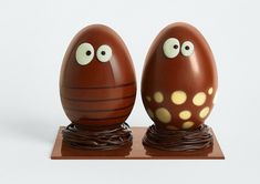 two chocolate eggs with googly eyes sitting on top of a wooden stand, one is brown and the other is white