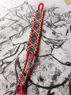 a red and green beaded lanyard on top of a white table with a drawing in the background