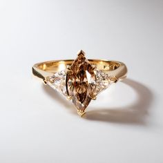 a gold ring with two pear shaped diamonds on it's sides and an orange diamond in the center