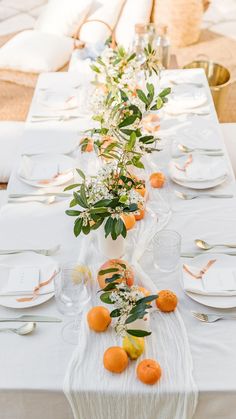 the table is set with white linens and oranges for an elegant dinner party