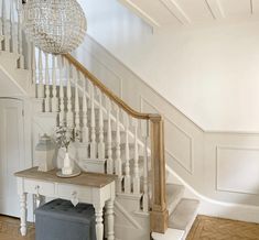 a white staircase with a bench under the bannister and a chandelier above it