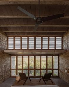 two chairs are in the middle of a room with large windows and wooden shutters