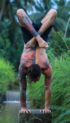 a man with tattoos doing a handstand in front of some bushes and trees