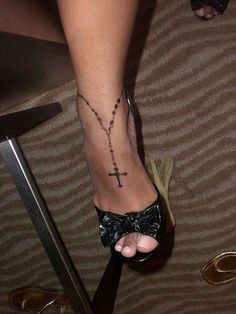 a woman's foot with a cross tattoo on her left ankle and a black bow tie around the ankle