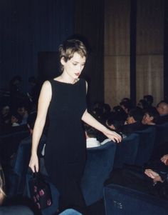 a woman in a black dress is walking through an auditorium with other people watching her