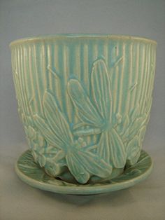 a green cup and saucer sitting on a white tableclothed surface with a flower design in the center