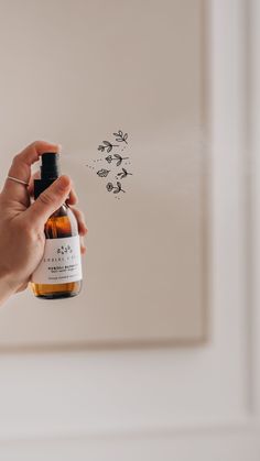 a hand holding a bottle of alcohol in front of a wall with bees drawn on it